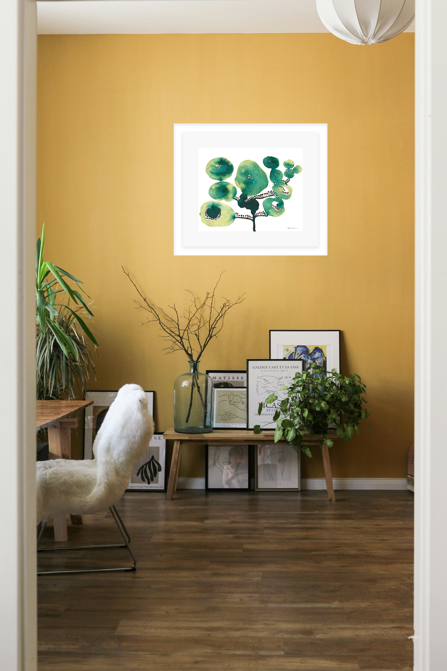 Living room with a yellow wall, framed artwork of green floral shapes on a white background