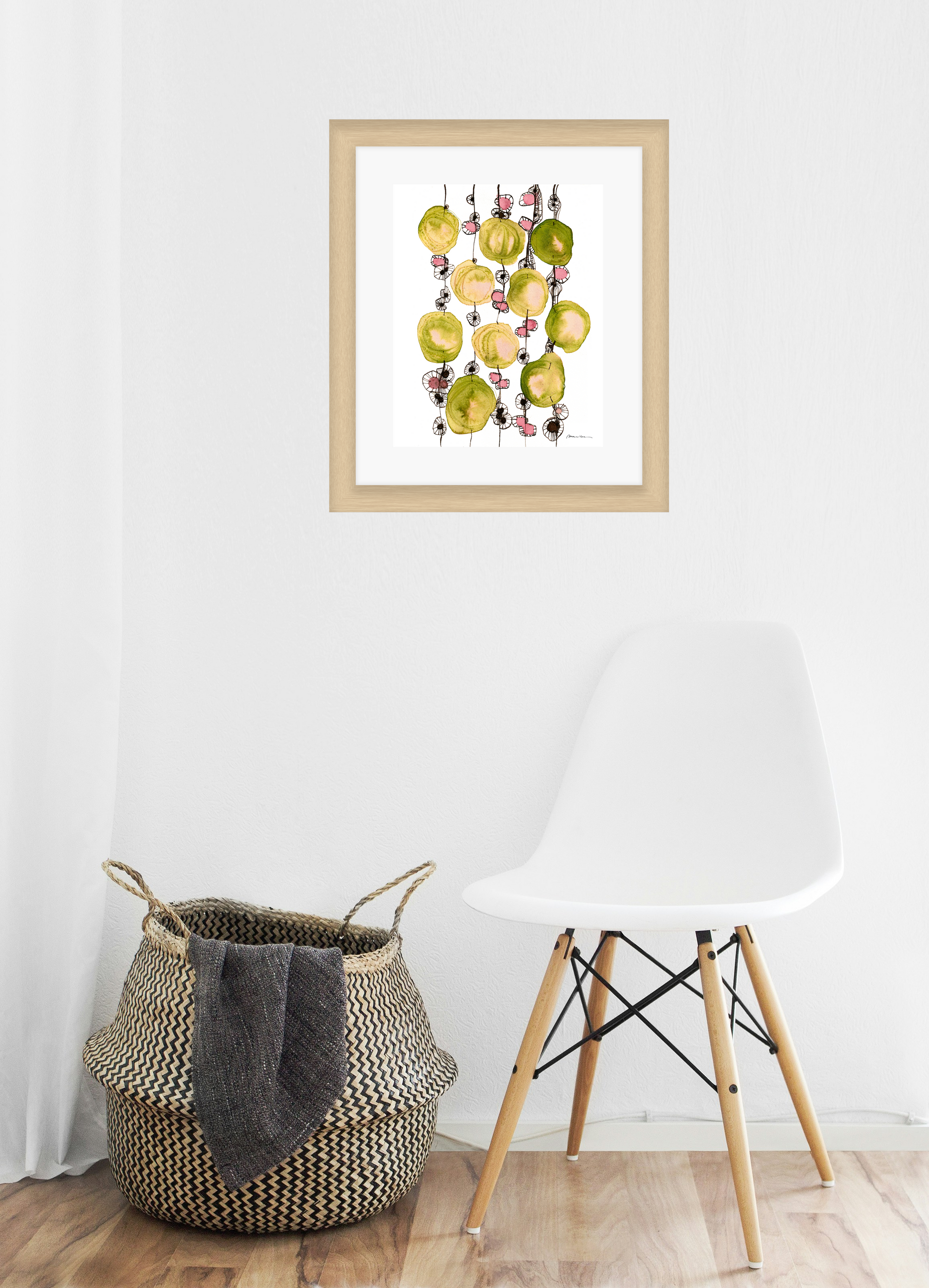Framed artwork of colorful shapes on a white wall above a woven basket and white chair.